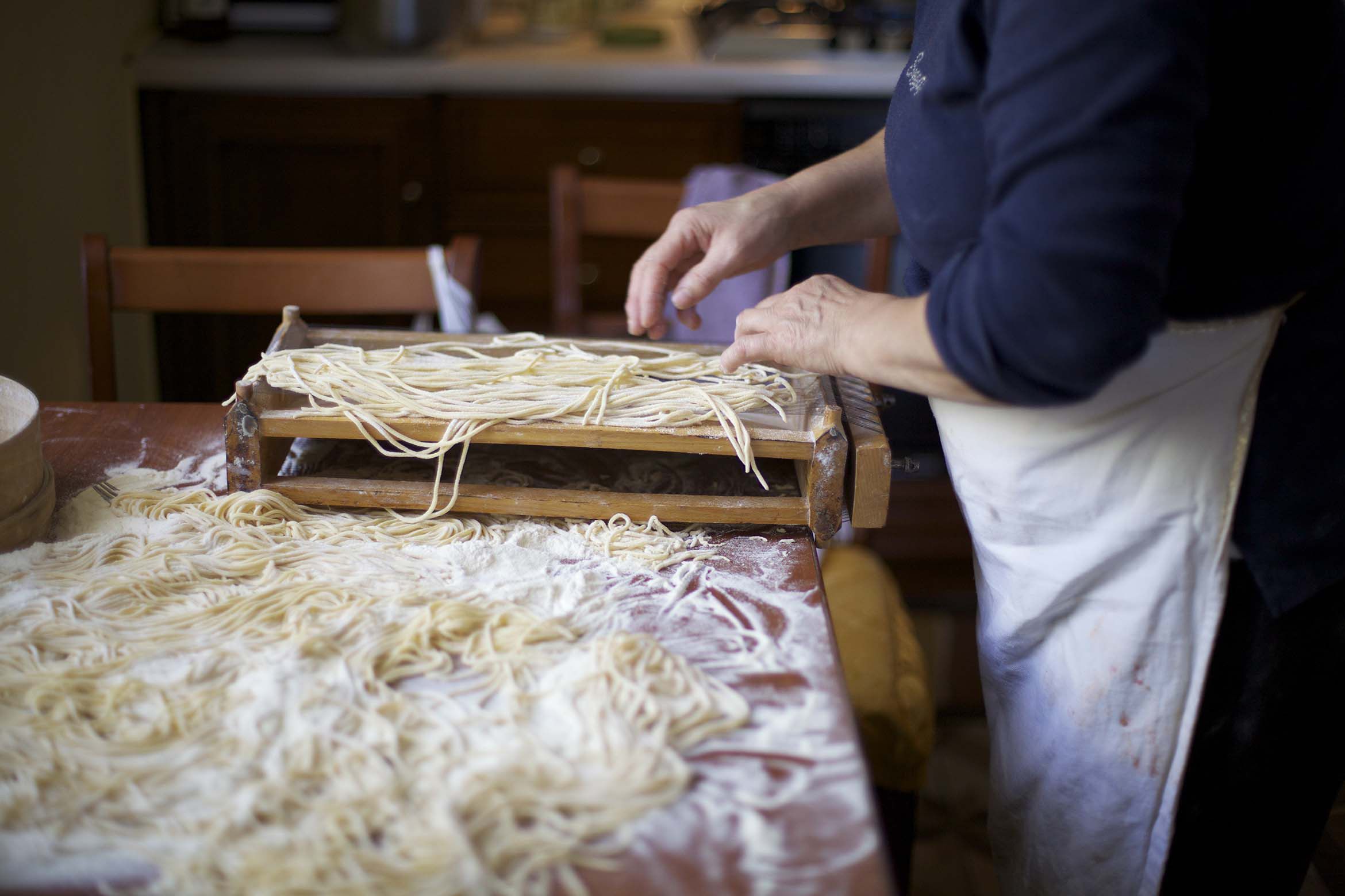 A person preparing pasta on a wooden board in a kitchen.