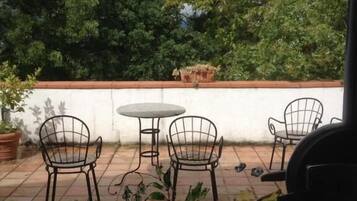 Un patio al aire libre con suelo de baldosas, sillas de metal, una mesa redonda y una planta en maceta.