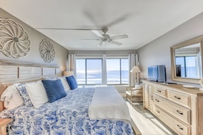 A bedroom with a large bed, a ceiling fan, a TV, and a view of the ocean.
