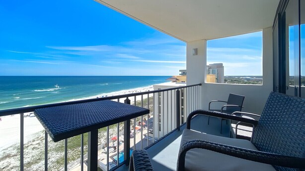 Un balcon avec vue sur l’océan et la plage, des meubles en osier et une petite table.