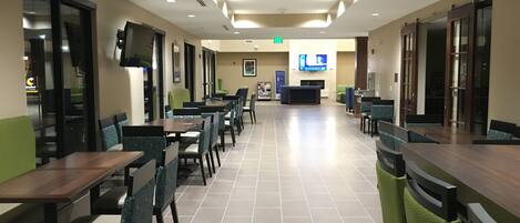 A spacious restaurant with multiple tables and chairs, a television mounted on the wall, and a tiled floor.