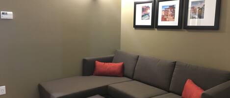 Ein modulares Sofa mit zwei roten Kissen, ein kleiner Hocker und drei gerahmte Bilder an der Wand.