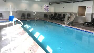 An indoor swimming pool with clear water, a diving board, and lounge chairs along the side.