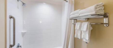 A modern bathroom with a white bathtub, a shower with a handheld showerhead, a grab bar, and a towel rack with folded towels.