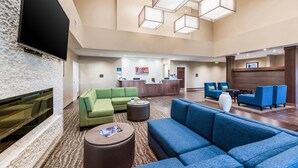 A spacious lobby with a reception desk, green and blue seating areas, a flat-screen TV mounted on a textured wall, and geometric pendant lighting. - Comfort Inn & Suites Zion Park Area (Hurricane)
