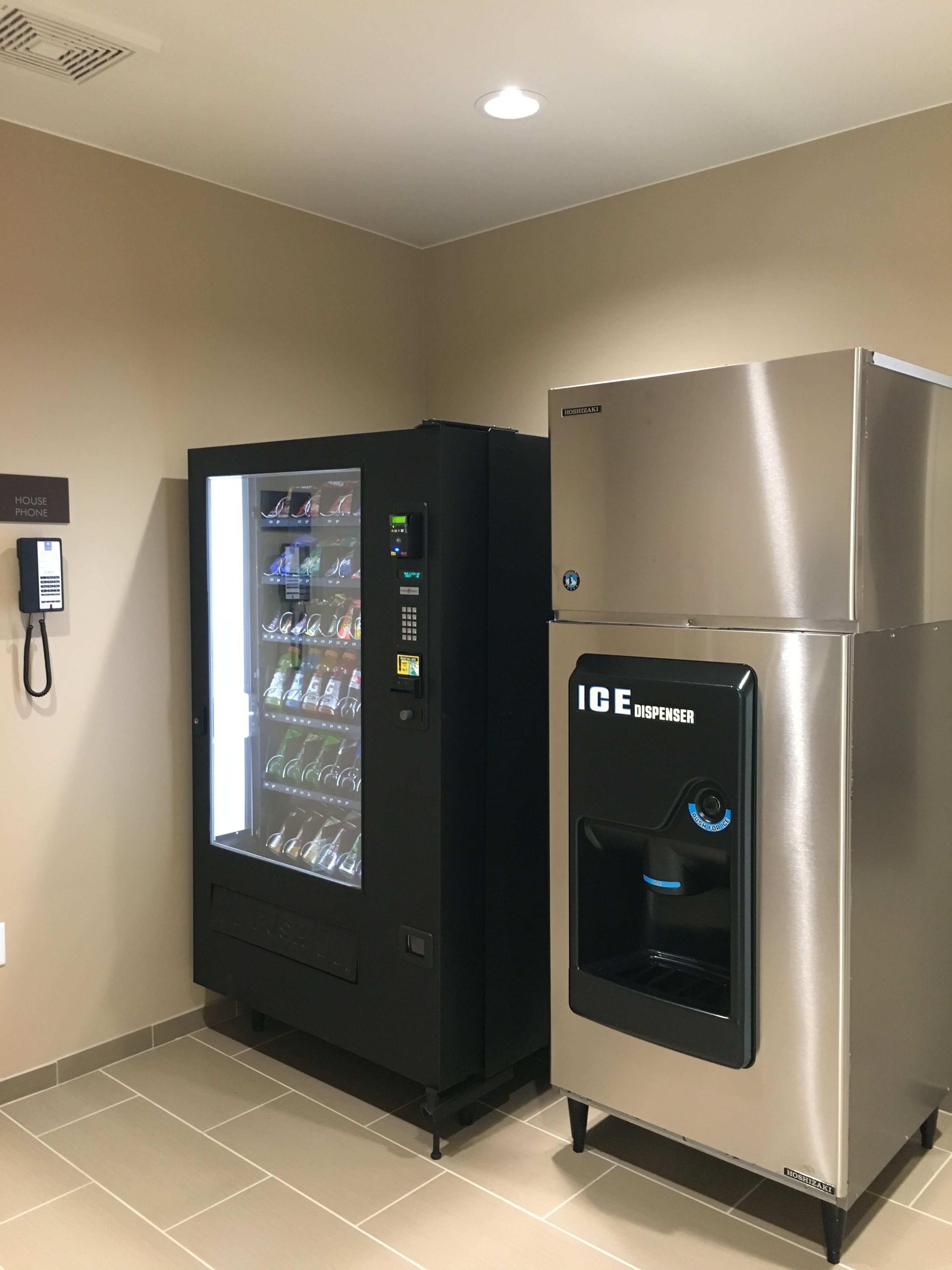 A vending machine and a refrigerator in a room with beige walls and tiled flooring.