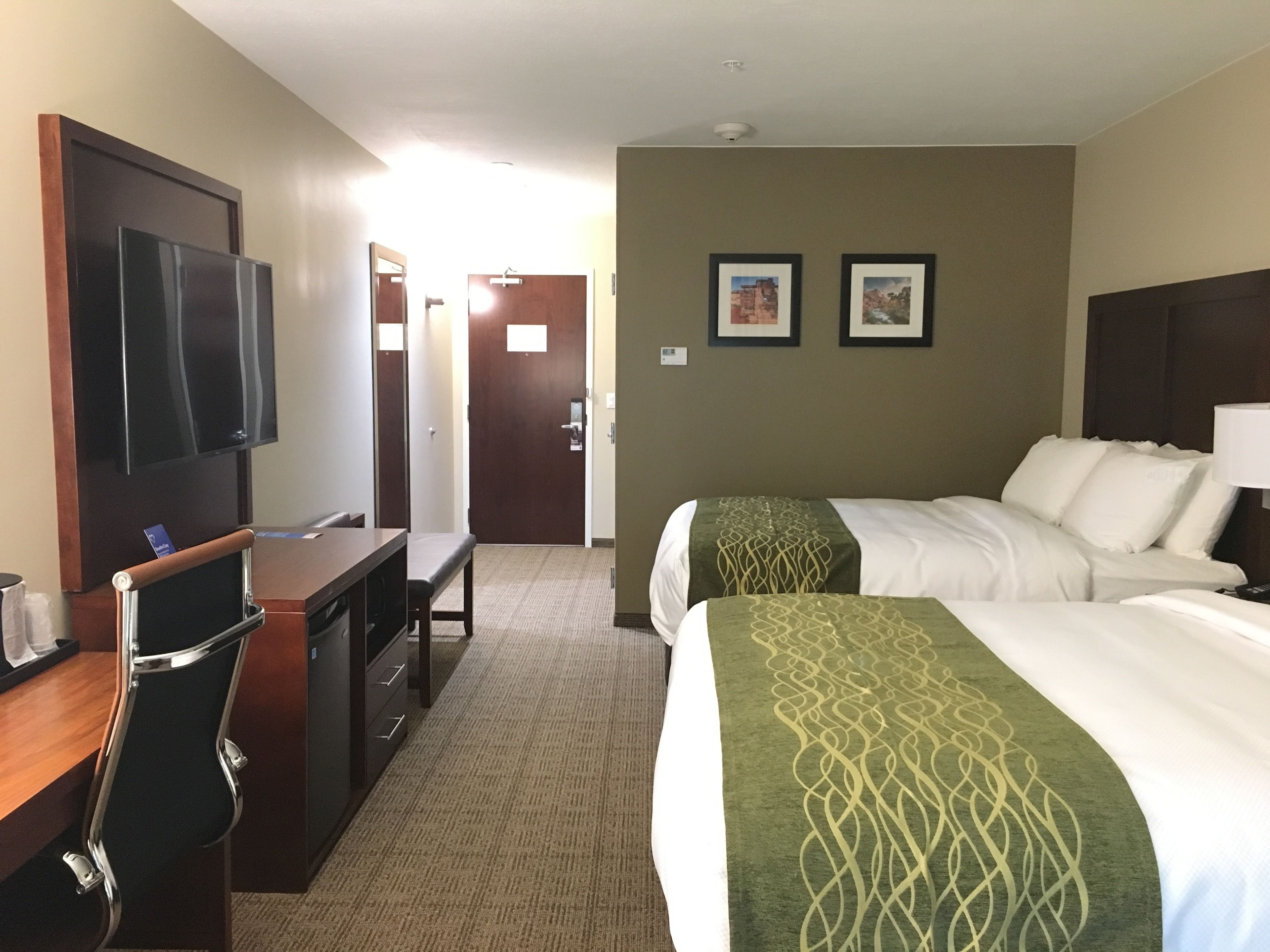 A hotel room with a bed, a desk, a chair, a television, and two framed pictures on the wall.