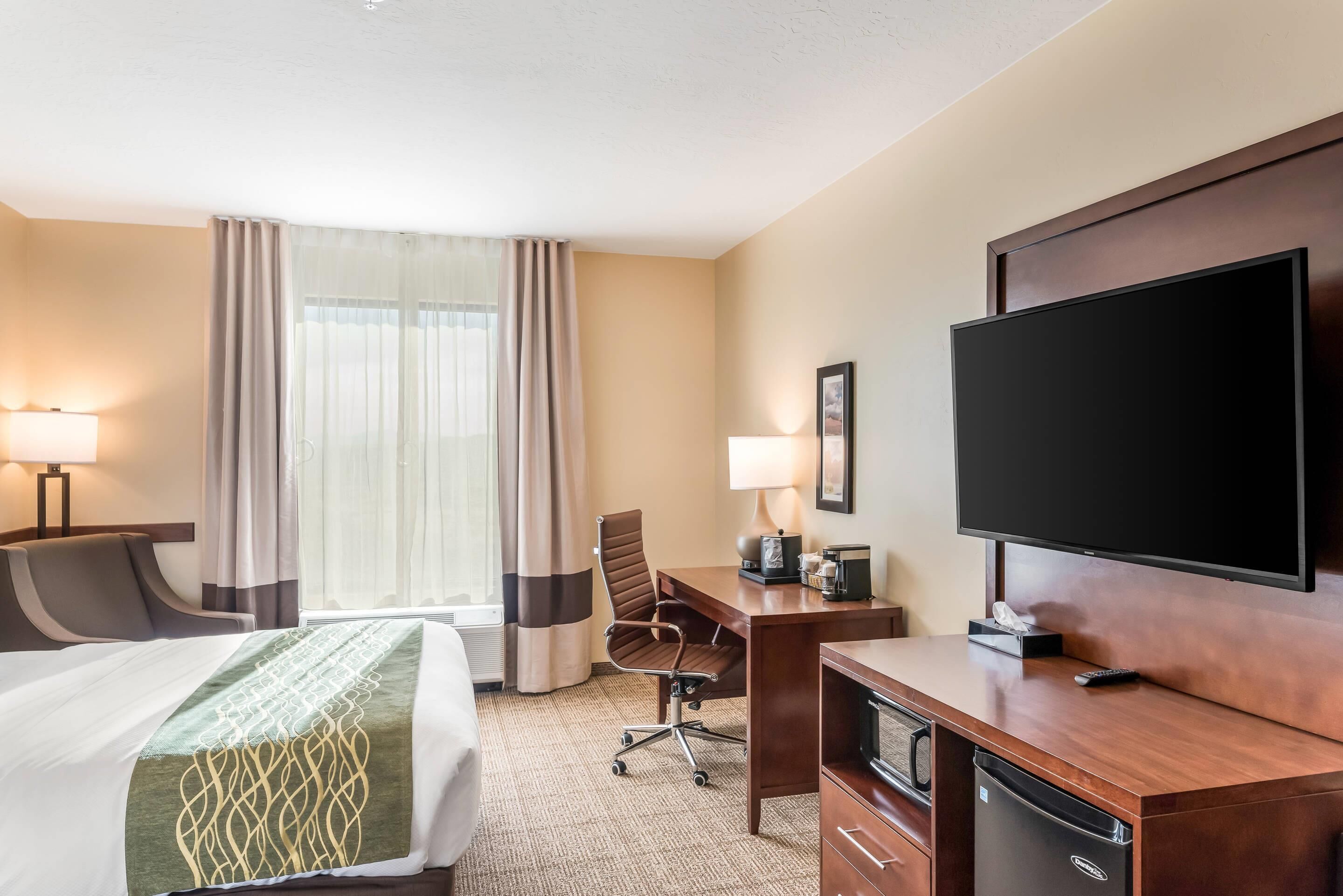 A hotel room with a bed, desk, TV, and a window with curtains.