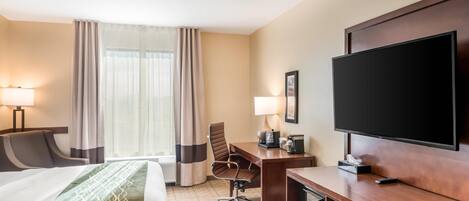A hotel room with a bed, desk, TV, and a window with curtains.