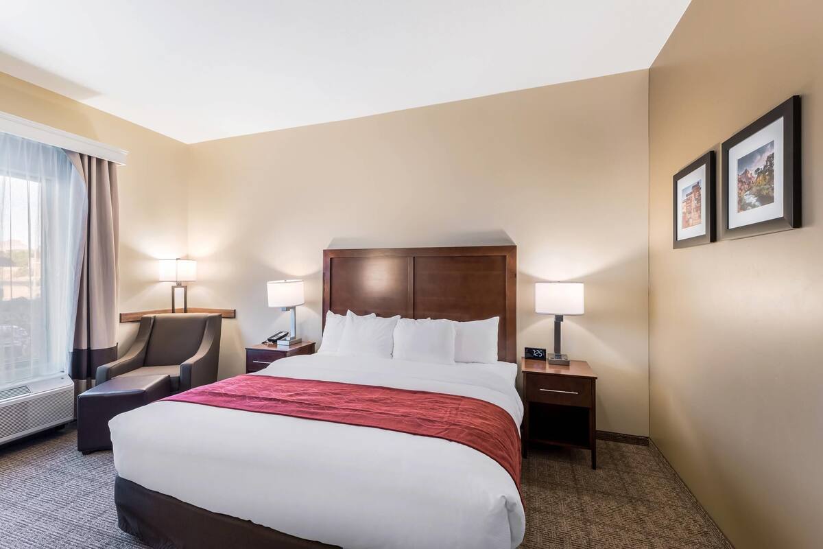 A hotel room with a large bed, a chair, two bedside tables with lamps, and a window with curtains.