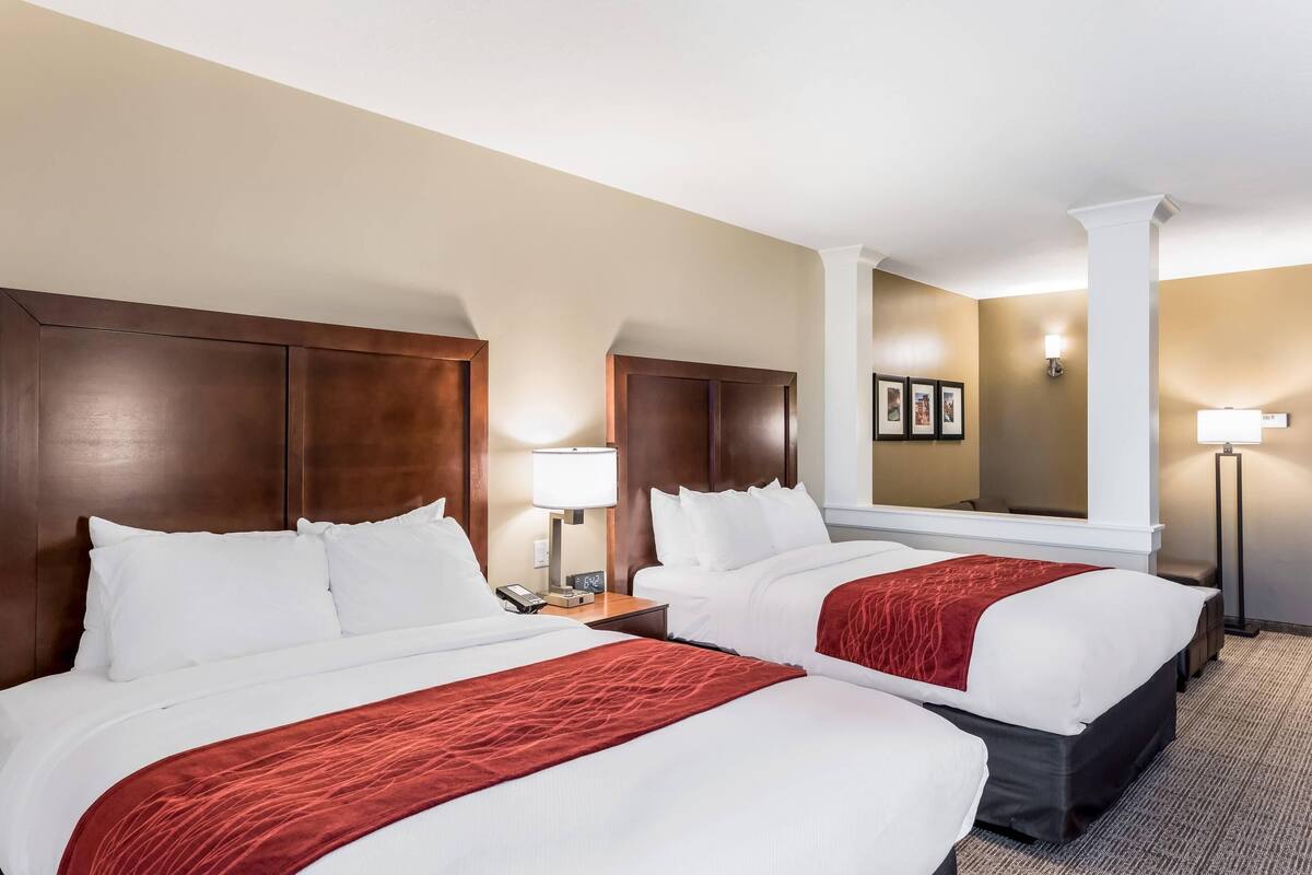 A hotel room with two beds, a wooden headboard, a nightstand with a lamp, and a mirror on the wall.