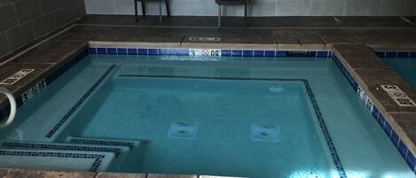 A swimming pool with blue tiles, two black chairs, and a tiled wall with a sign.