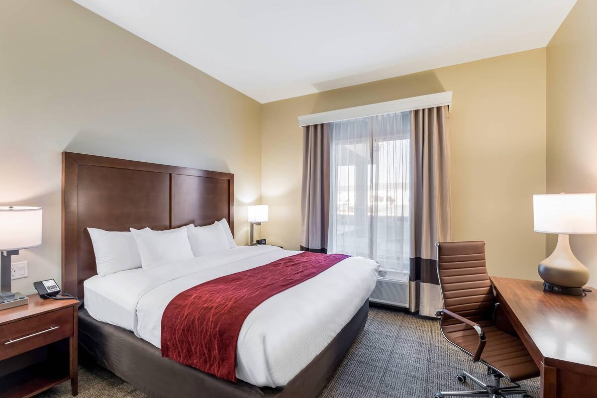 A hotel room with a large bed, a desk with a chair, a telephone, and a window with curtains.