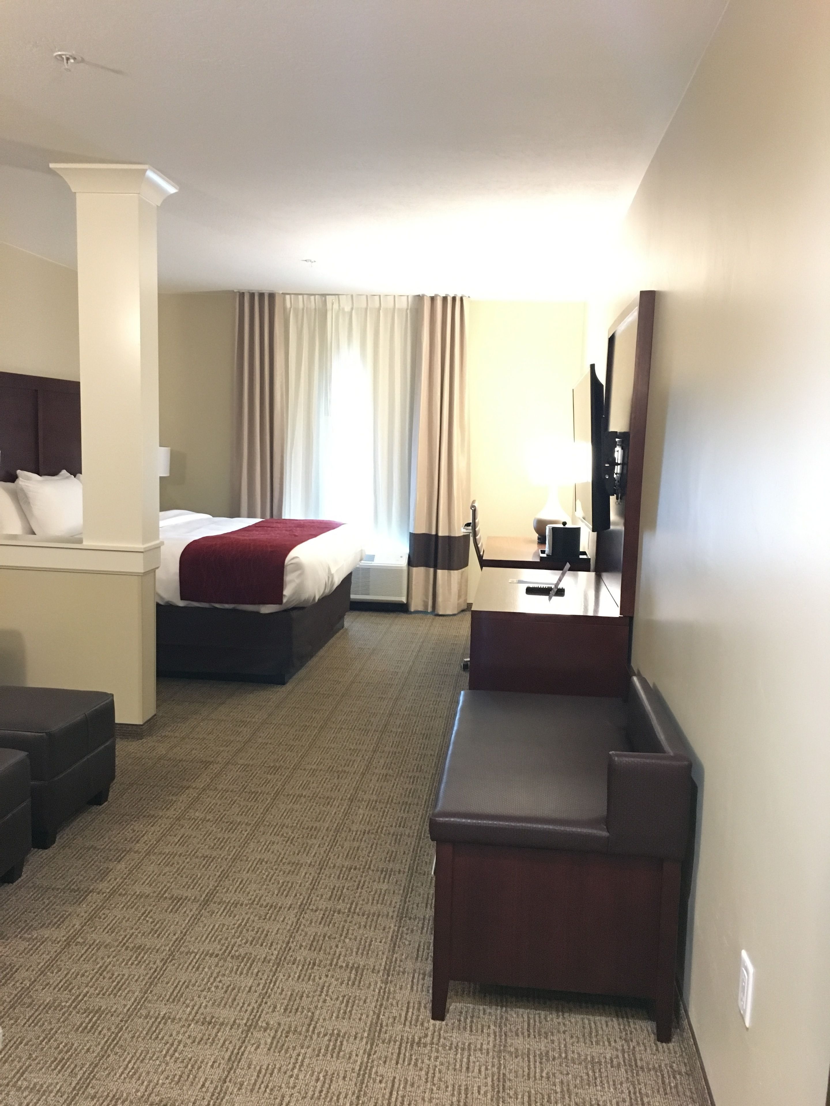 A hotel room with a bed, a desk, a chair, a sofa, and a mirror.