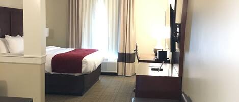 A hotel room with a bed, a desk, a chair, a sofa, and a mirror.