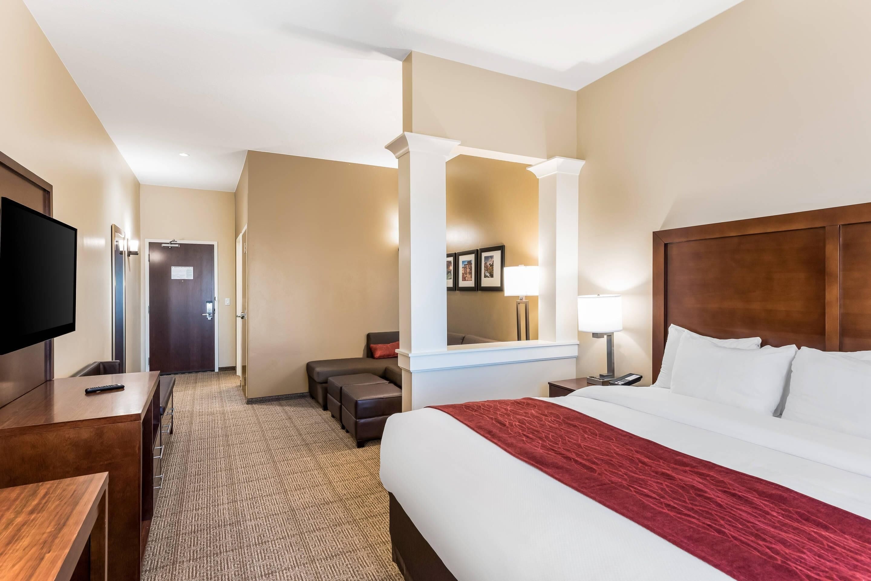 Una habitación de hotel con una cama grande, televisión, escritorio, silla, sofá y espejo.