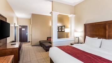 Une chambre d’hôtel avec un grand lit, une télévision, un bureau, une chaise, un canapé et un miroir.