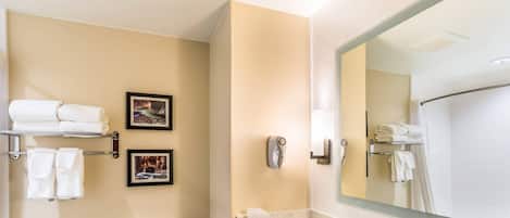 A modern bathroom with a toilet, sink, and large mirror. There are towels on a rack and a picture frame on the wall.