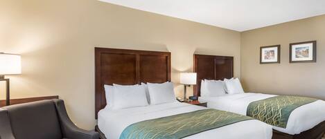 Quarto de hotel com duas camas, uma escrivaninha, uma cadeira e uma luminária.