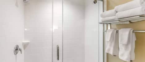 A glass-enclosed shower with a chrome showerhead, a glass door, and a towel rack with folded towels.