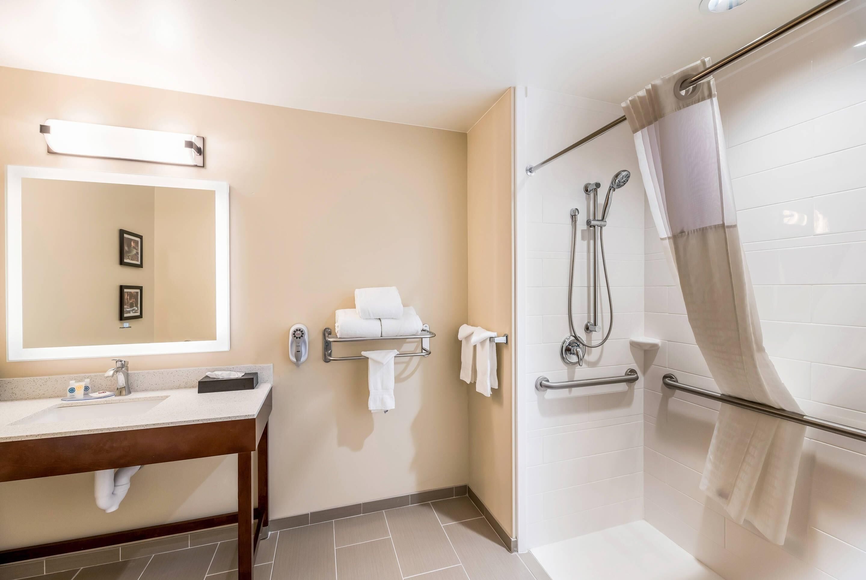 Une salle de bain équipée d’un lavabo, d’un miroir, d’un porte-serviettes, d’une douche et de toilettes.