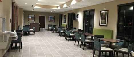 A spacious indoor area with multiple tables and chairs, a reception desk, and a television mounted on the wall.