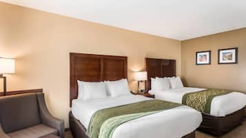 A hotel room with two beds, a chair, a nightstand with a lamp, and two framed pictures on the wall.