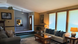 A living room with a sofa, coffee table, and a rug. There is a door leading to another room, a lamp, and a window with blinds. - Spokane Indoor Pool Home (Spokane)