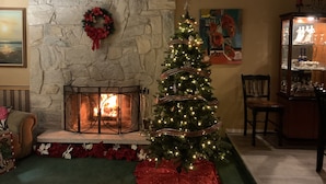 A cozy living room with a fireplace, a Christmas tree, and a stone wall. - Spokane Indoor Pool Home (Spokane)