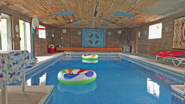 An indoor swimming pool with wooden ceiling and walls, a colorful mural, and inflatable rings. - Spokane Indoor Pool Home (Spokane)