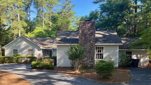 A two-story house with a stone chimney, a front porch, and a driveway leading to the entrance. - Golfers getaway - putting green, billiards, bar, arcade , poker table and more (Pinehurst)