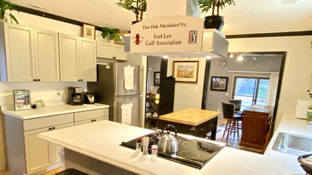 A modern kitchen with white cabinets, a central island with stools, a stove, and a sign indicating the hotel is marshall by Fort Lee Golf Association. - Golfers getaway - putting green, billiards, bar, arcade , poker table and more (Pinehurst)