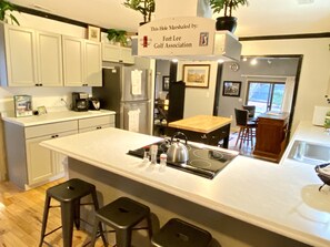 A modern kitchen with white cabinetry, a central island with stools, a built-in stove, and a sign indicating the hotel is associated with Fort Lee Golf Association. - Golfers getaway - putting green, billiards, bar, arcade , poker table and more (Pinehurst)
