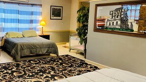 A bedroom with a bed, a nightstand, a lamp, a framed picture, a window with curtains, and a wall-mounted picture of a building. - Golfers getaway - putting green, billiards, bar, arcade , poker table and more (Pinehurst)