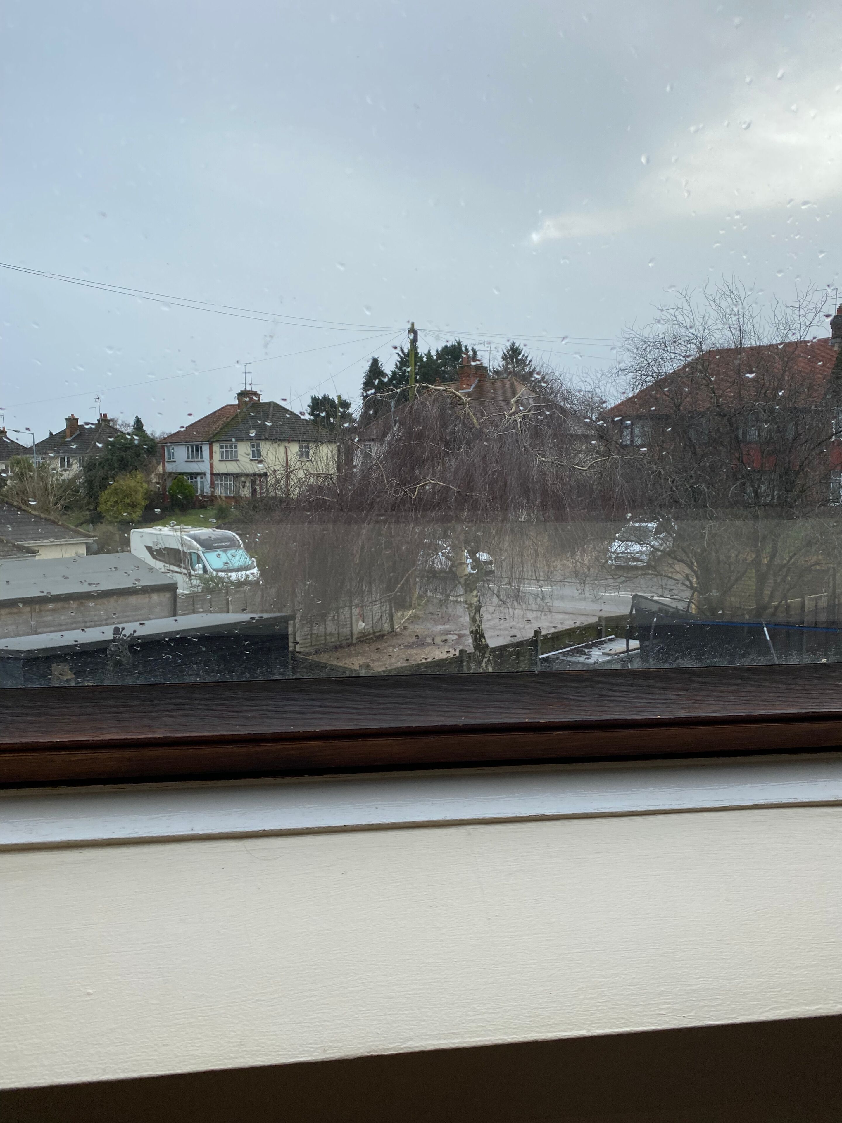 A view from a window with raindrops, including houses, a tree, and a parked car.