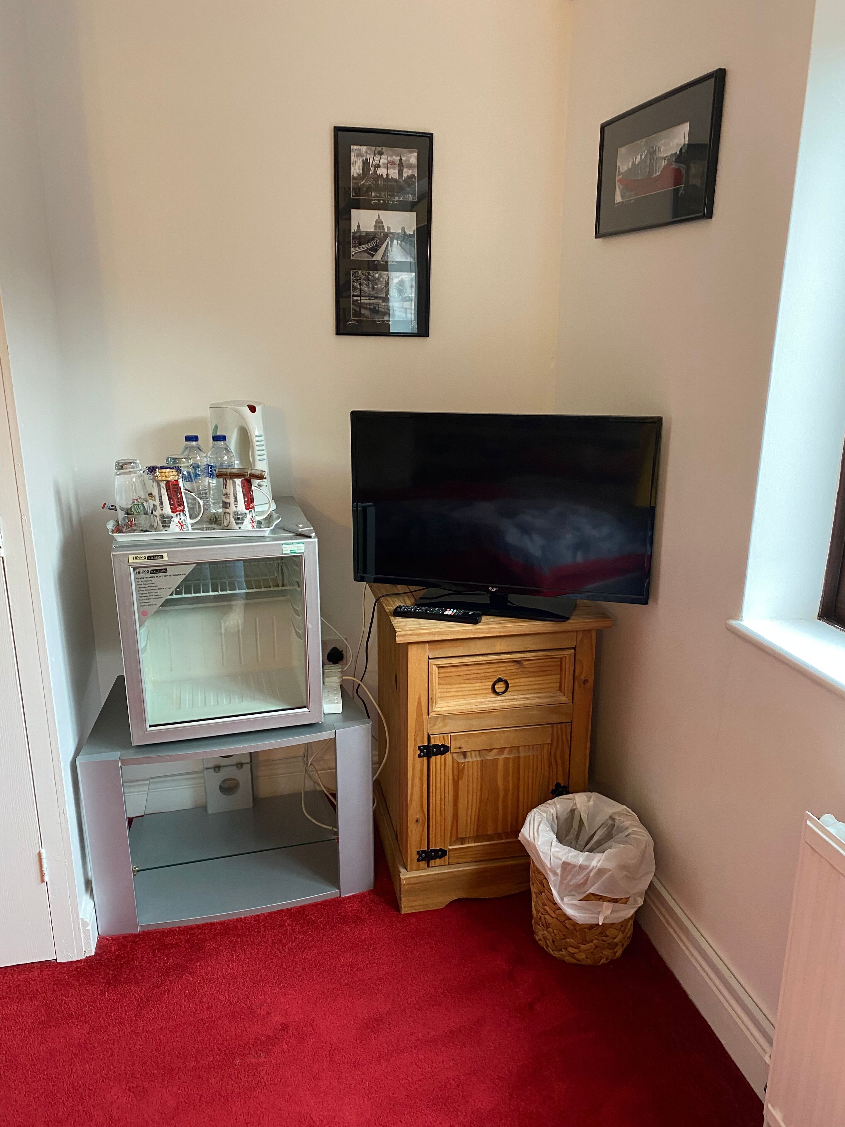 A room with a television, a microwave, a cabinet, and a trash bin.