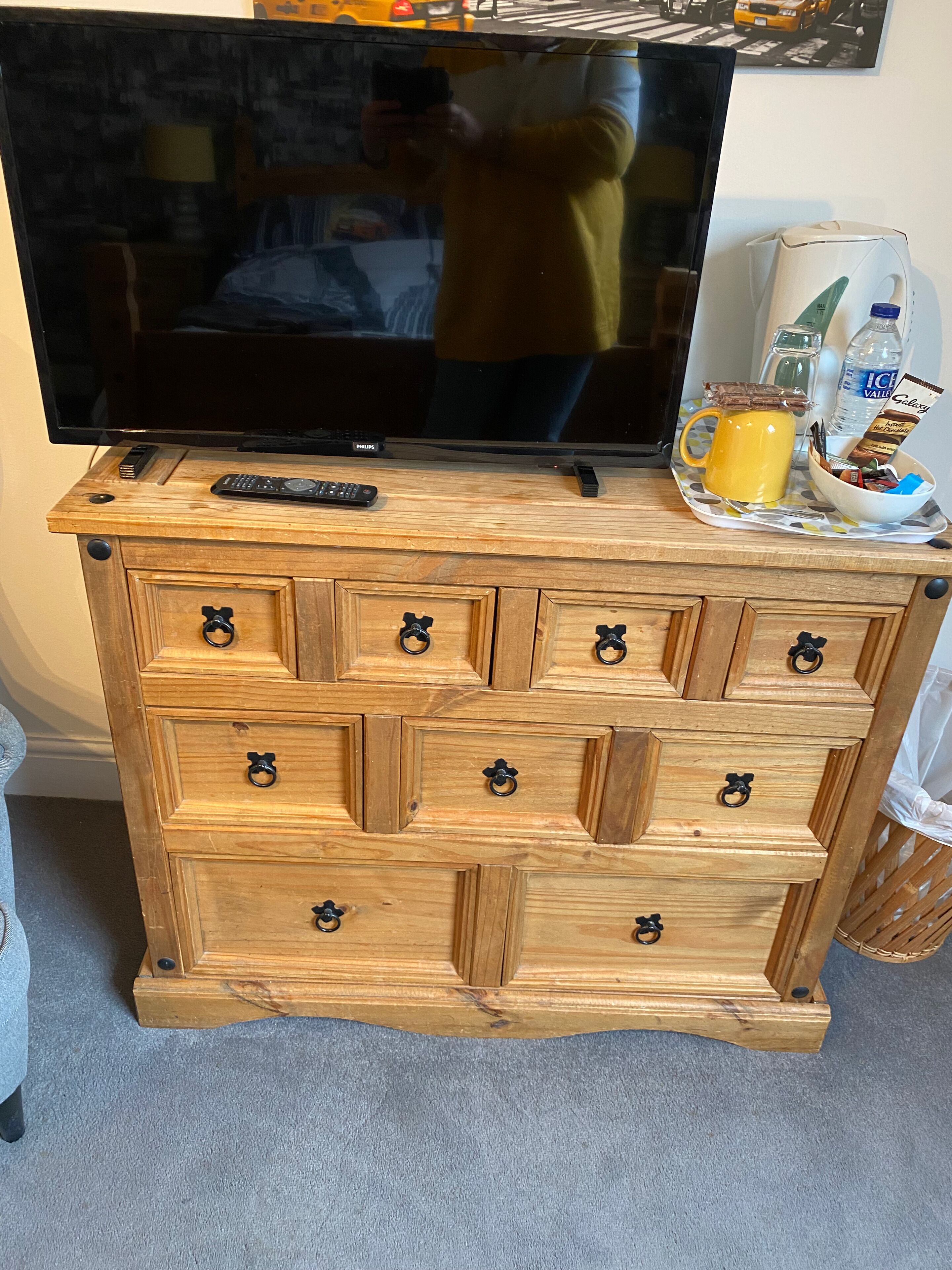 Un mueble de madera con varios cajones, un televisor encima y una bandeja con una taza y aperitivos.