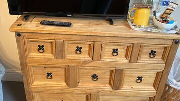Un mueble de madera con varios cajones, un televisor encima y una bandeja con una taza y aperitivos.
