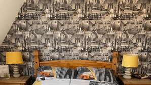 A bedroom with a cityscape bedspread, wooden headboard, two bedside tables with lamps, and a nightstand with a lamp and a menu. - Rosebarne Bed & Breakfast (Haverhill)