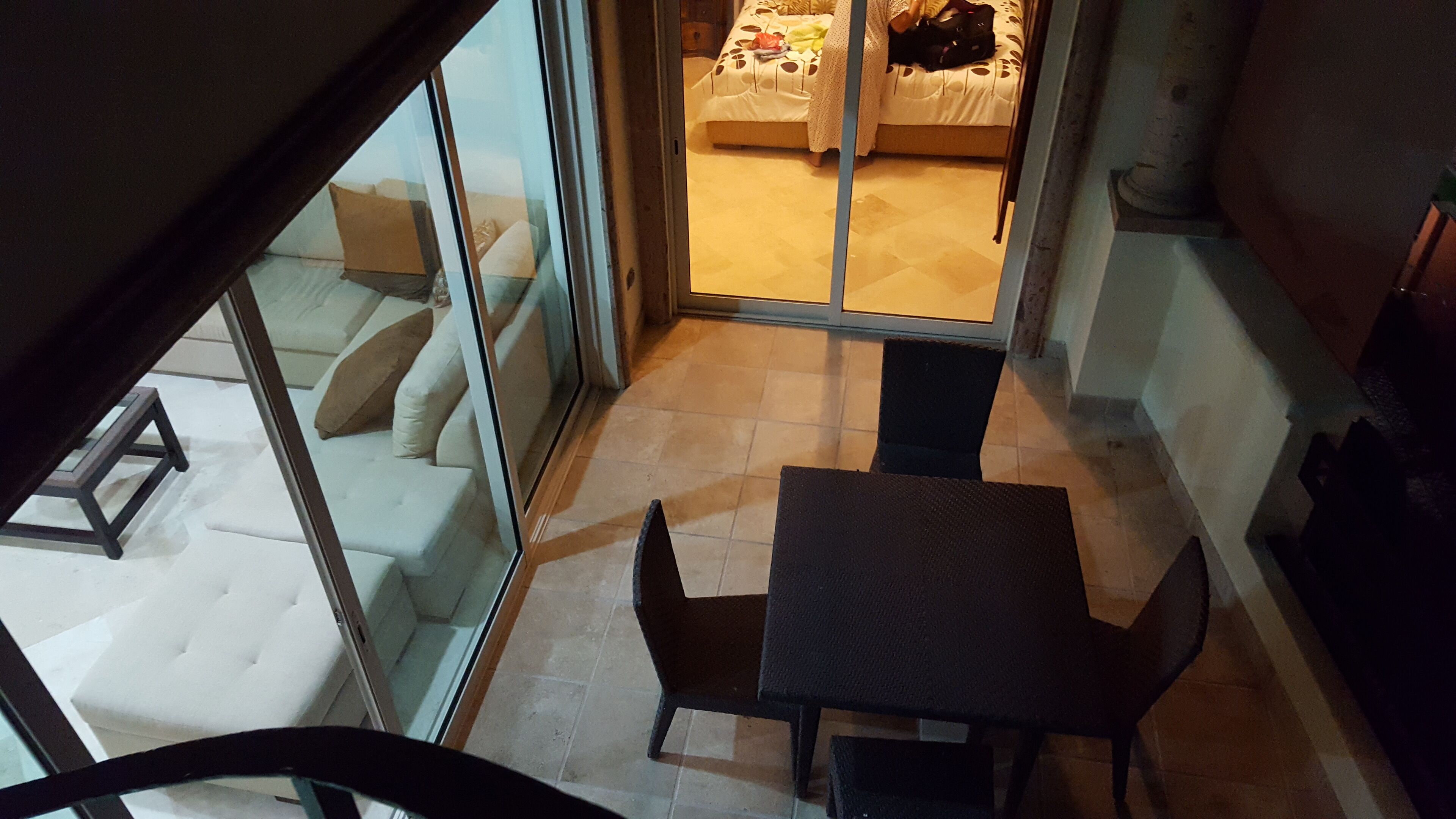 A small balcony with a table and chairs, a sofa with cushions, and a bed with a patterned bedspread.