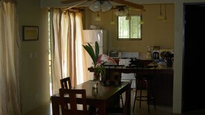 A dining area with a table, chairs, a ceiling fan, and a kitchen in the background. - Sublime Obsession-Amazing Views & Sunsets on the Pacific Ocean (Coyote)