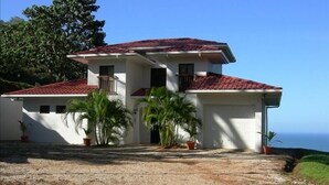 A two-story house with a red-tiled roof, white walls, and a garage. There are two potted plants in front of the house. - Sublime Obsession-Amazing Views & Sunsets on the Pacific Ocean (Coyote)