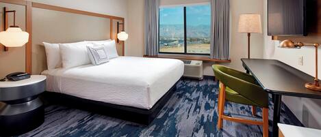 A hotel room with a bed, a desk, a chair, a TV, and a window with a mountain view.