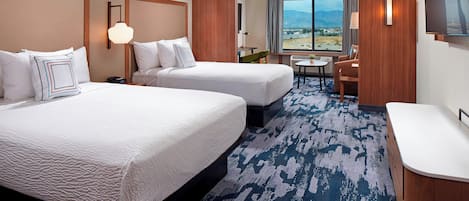 A hotel room with two beds, a desk, a chair, a TV, and a large window with a view.