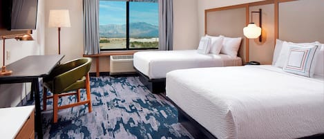 A hotel room with two beds, a desk, a chair, a TV, and a large window with a mountain view.