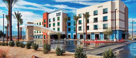 A modern hotel with a pool area, palm trees, and a clear blue sky.