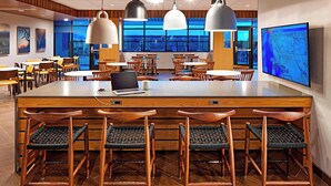 A modern restaurant with wooden tables and chairs, a bar area, and a large TV screen displaying a map. - Fairfield by Marriott Inn & Suites Indio Coachella Valley (Indio)