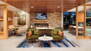 A modern living room with a stone fireplace, comfortable seating, a flat-screen TV, and a dining area with wooden furniture. - Fairfield by Marriott Inn & Suites Indio Coachella Valley (Indio)