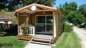 A small, single-story wooden cabin with a porch and a sliding glass door. - Camping Saint Paul (Lyons-la-Foret)