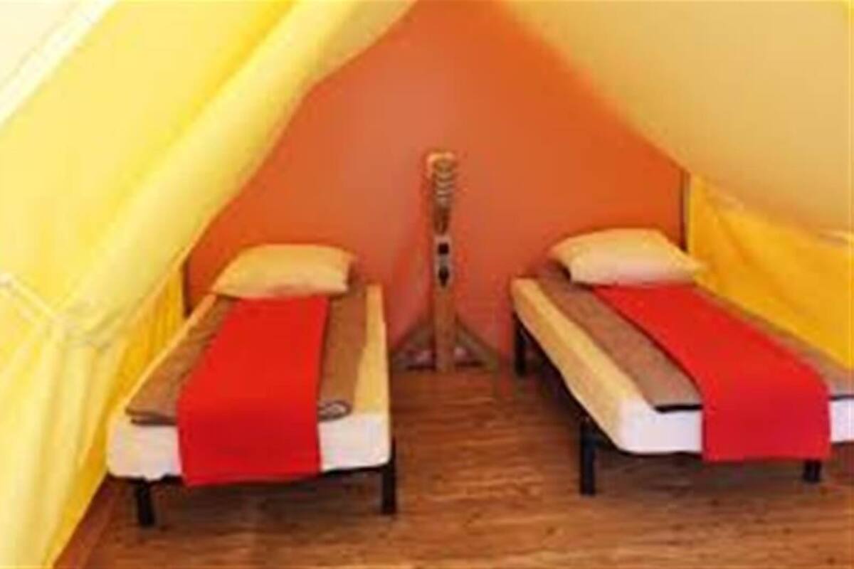 Una habitación pequeña y privada con dos camas, cada una con una colcha roja y almohadas blancas.